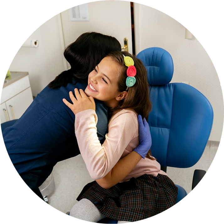 Female Doctor Hugging Young Female Smiling Patient Sitting In Examination Chair