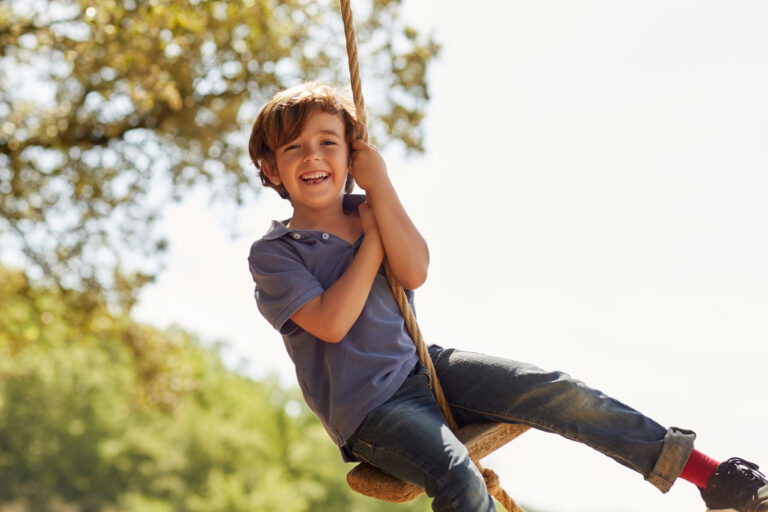Happy Boy Playing On Swing Against Sky