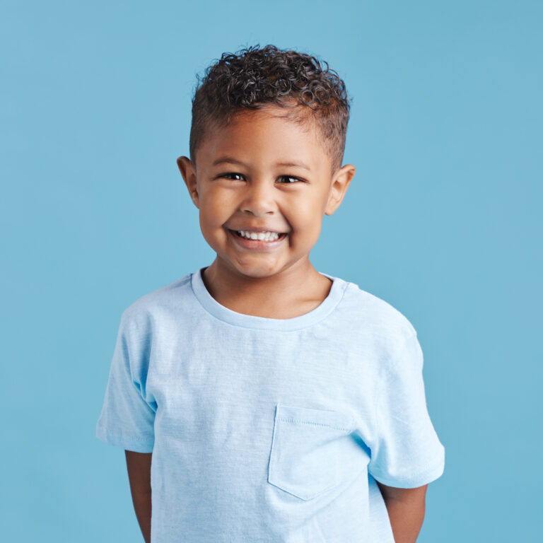 Portrait Of A Smiling Little Brown Haired Boy Looking At The Camera. Happy Kid With Good Healthy Teeth For Dental On Blue Background