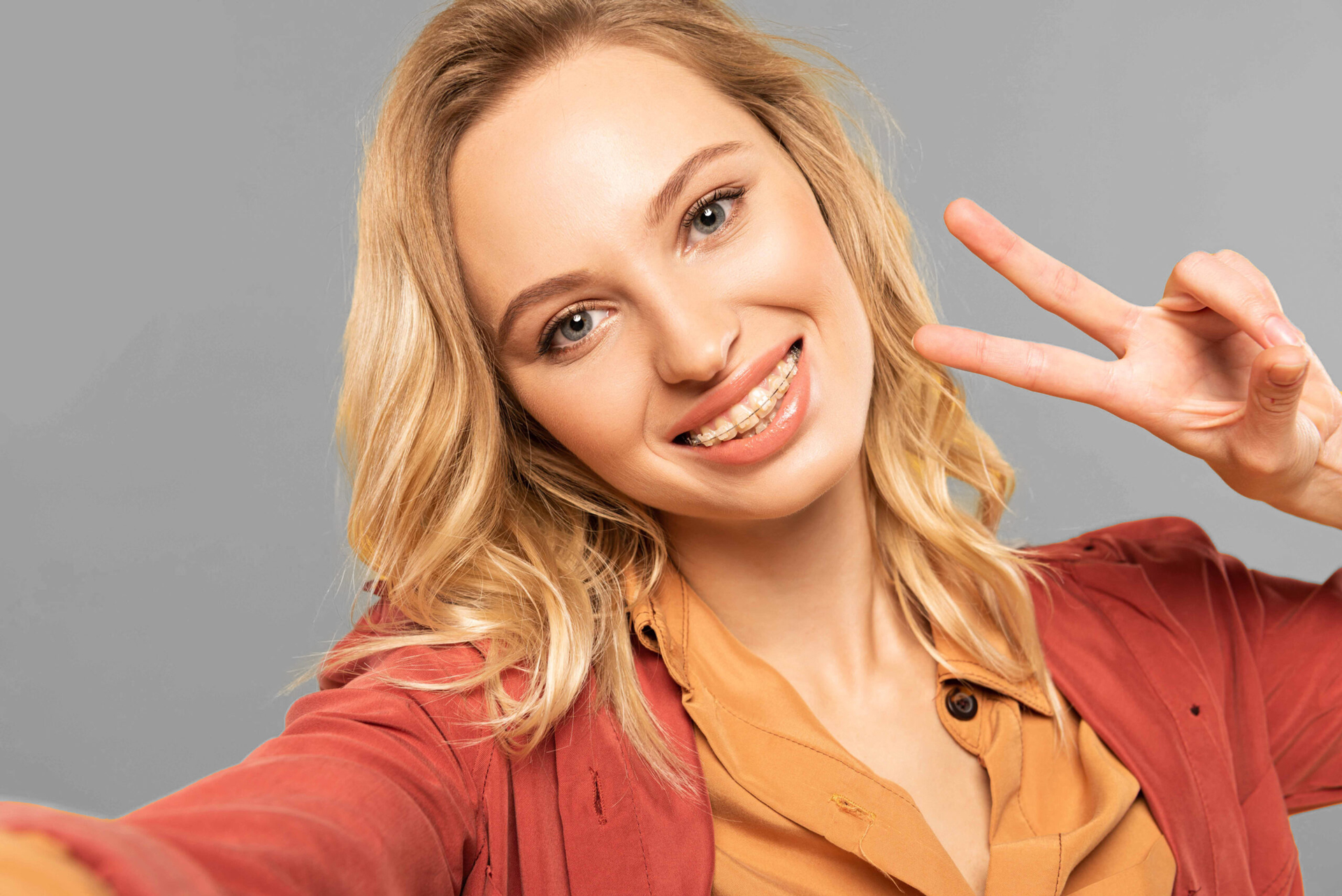 Woman Wearing Braces Holding Up Two Fingers Making Peace Sign