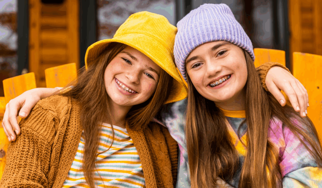 Two young friends with auburn hair and braces smiling in an oversized chair together while embracing