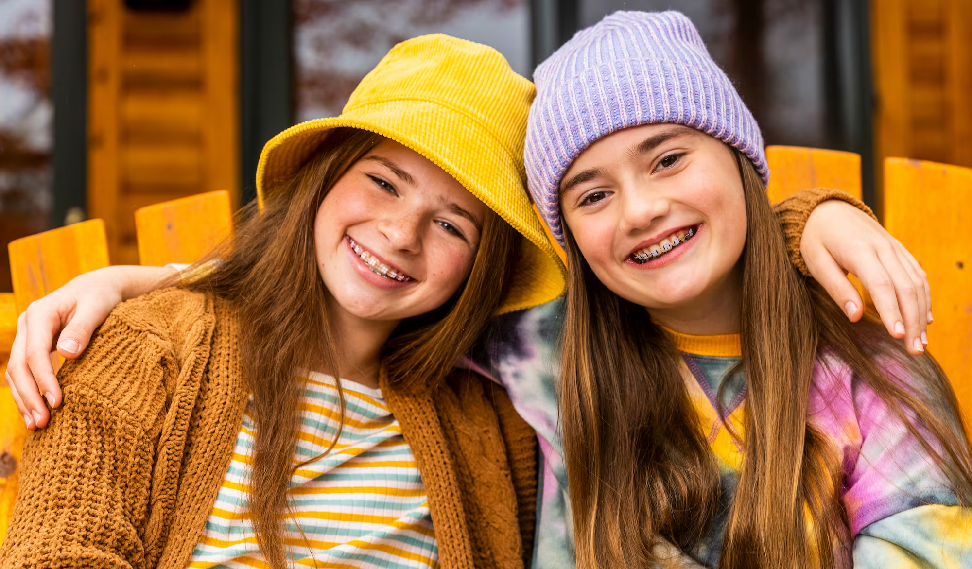 Two young friends with auburn hair and braces smiling in an oversized chair together while embracing